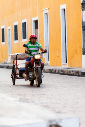 A friendly mototaxi driver helping a passenger with a helmet in a vibrant city street.