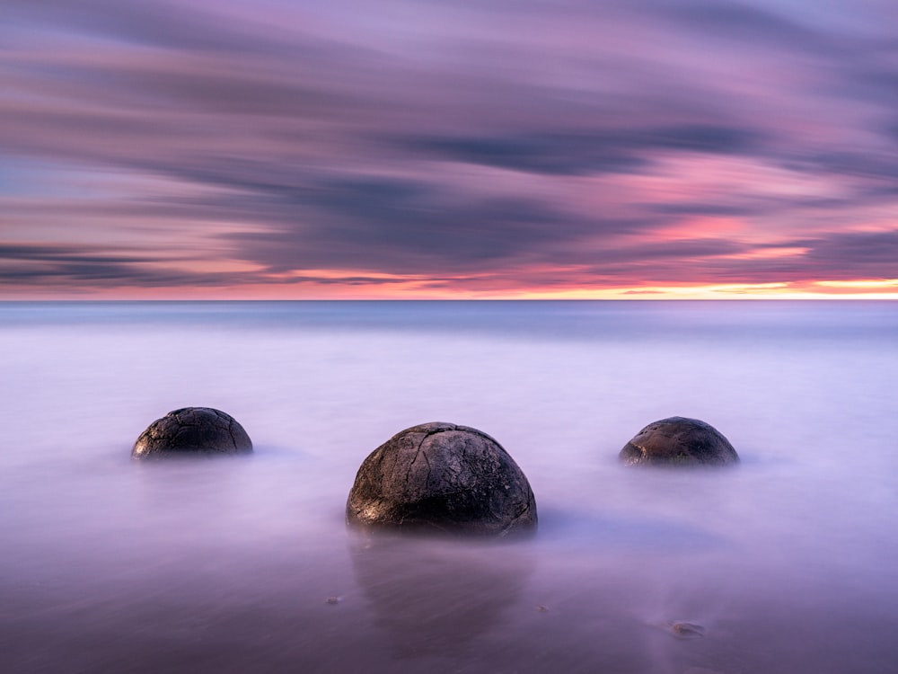 black rock on body of water during sunset