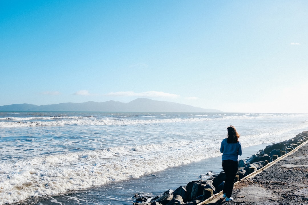 man in black jacket standing on rock near body of water during daytime