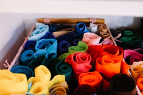 A basket filled with neatly arranged rolls of colorful felt fabric. The fabrics are rolled tightly and organized by color, creating a vibrant and visually appealing display. Shades range from blues and greens to reds, oranges, and yellows.
