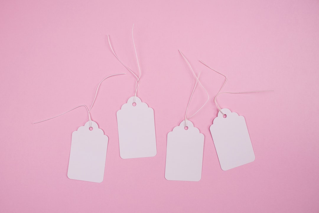 white apple earpods on pink surface, White paper hang tags against pastel pink background with copy space. Ideal for sal