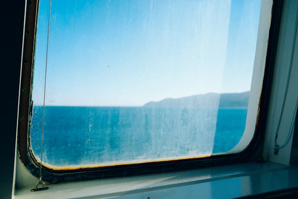 A professional cleaner polishing a large window overlooking the Mediterranean coastline at sunset.