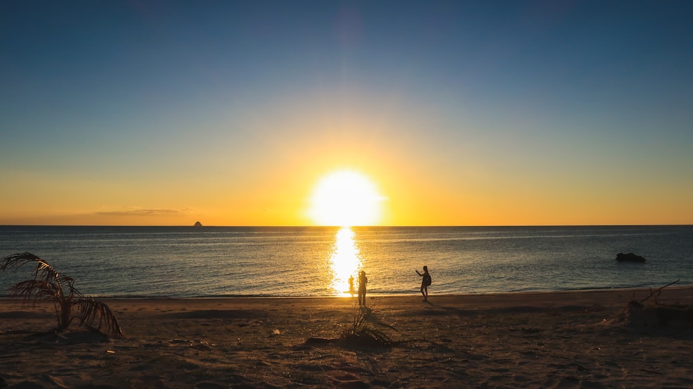 Silueta de 2 personas de pie en la playa durante la puesta del sol