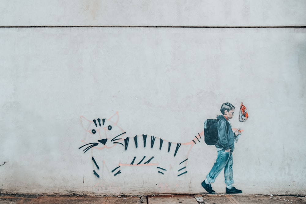 man in black jacket and pants standing beside wall with dog graffiti