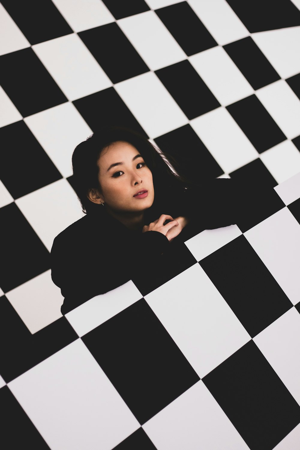 girl in black long sleeve shirt lying on black and white checkered floor