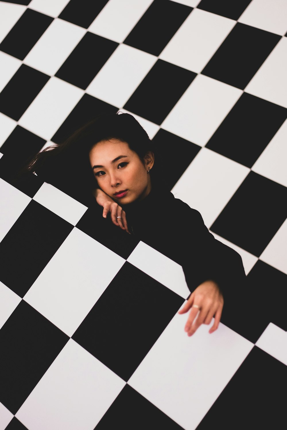 girl in black long sleeve shirt lying on black and white checkered floor