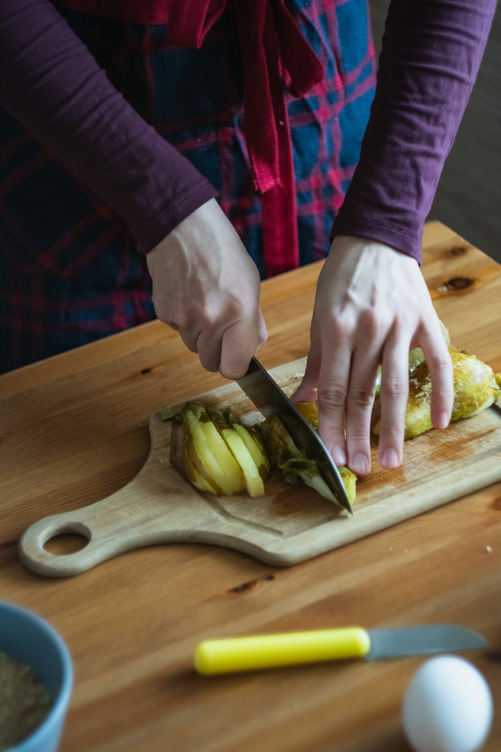 person slicing green vegetable on brown wooden chopping board