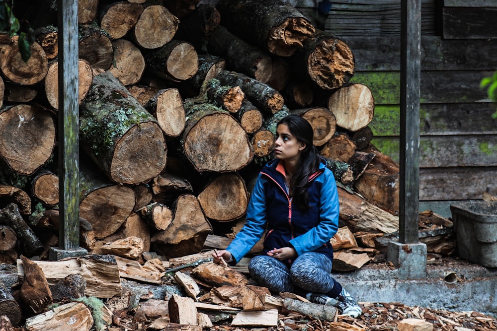 woman in blue jacket sitting on brown wood log