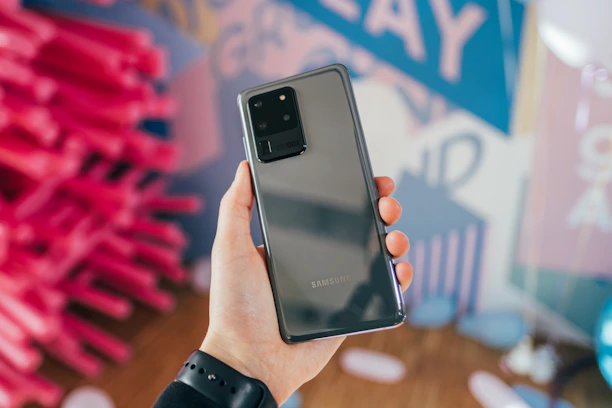 Happy customer holding a Samsung phone with a stylish charger visible on a light pastel backdrop.