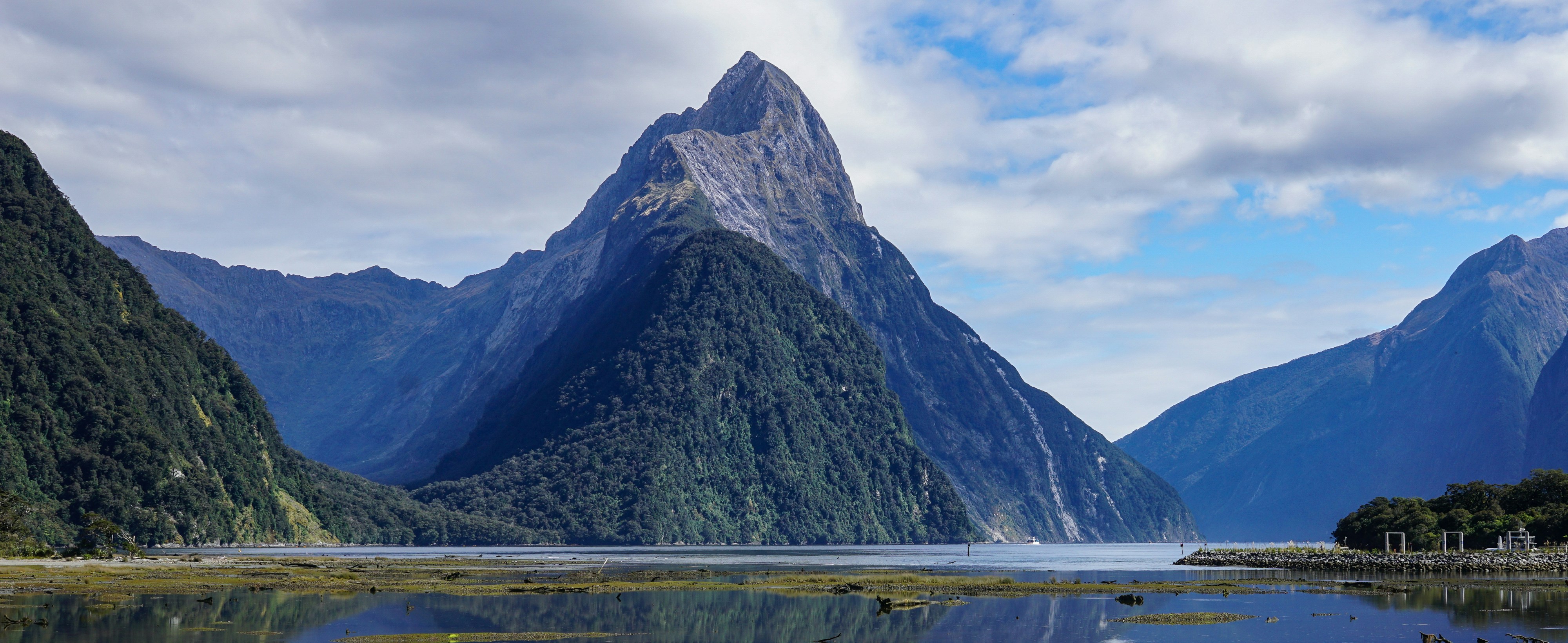 a lake surrounded by mountains under a cloudy blue sky, Mitre Peak, Milford Sound, New Zealand