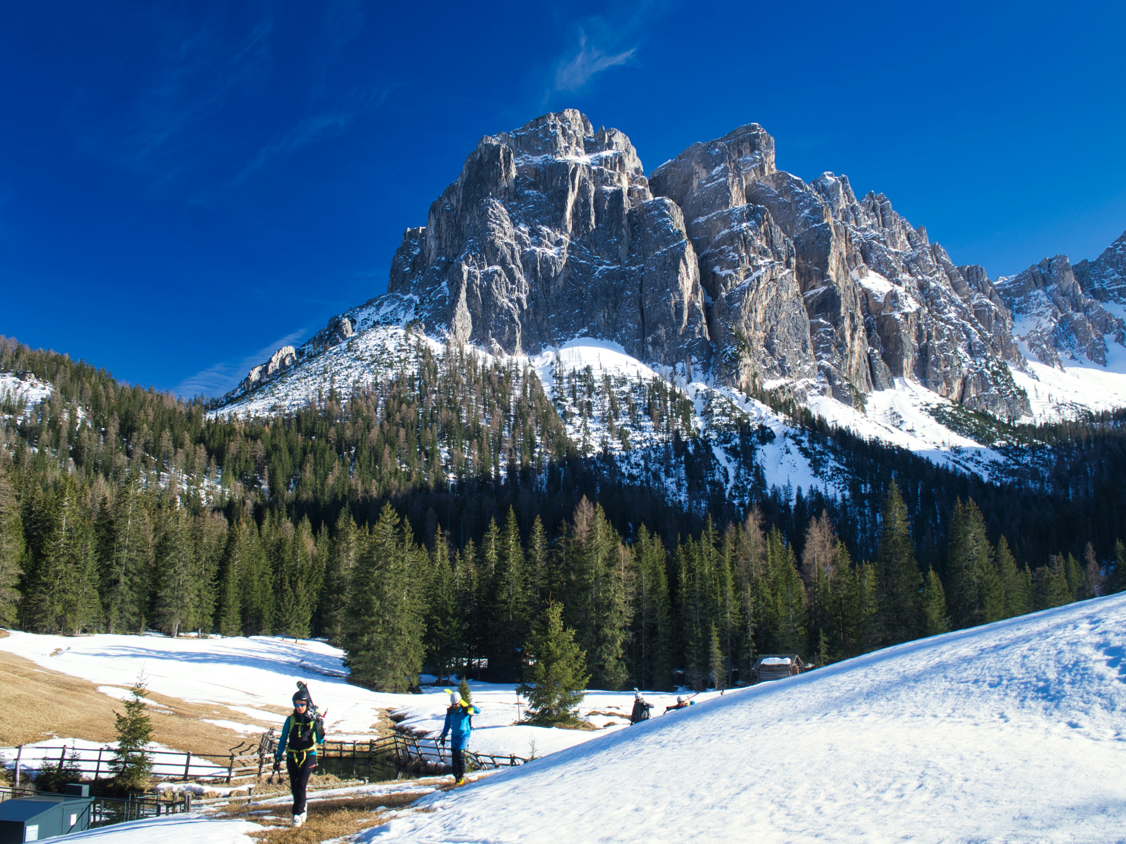 person walking on snow covered field near green trees and mountain under blue sky during daytime