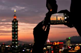 Stylish male influencer capturing city skyline views from a luxury hotel rooftop at dusk.