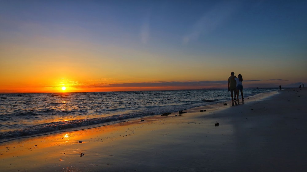 silhouette of 2 people walking on beach during sunset