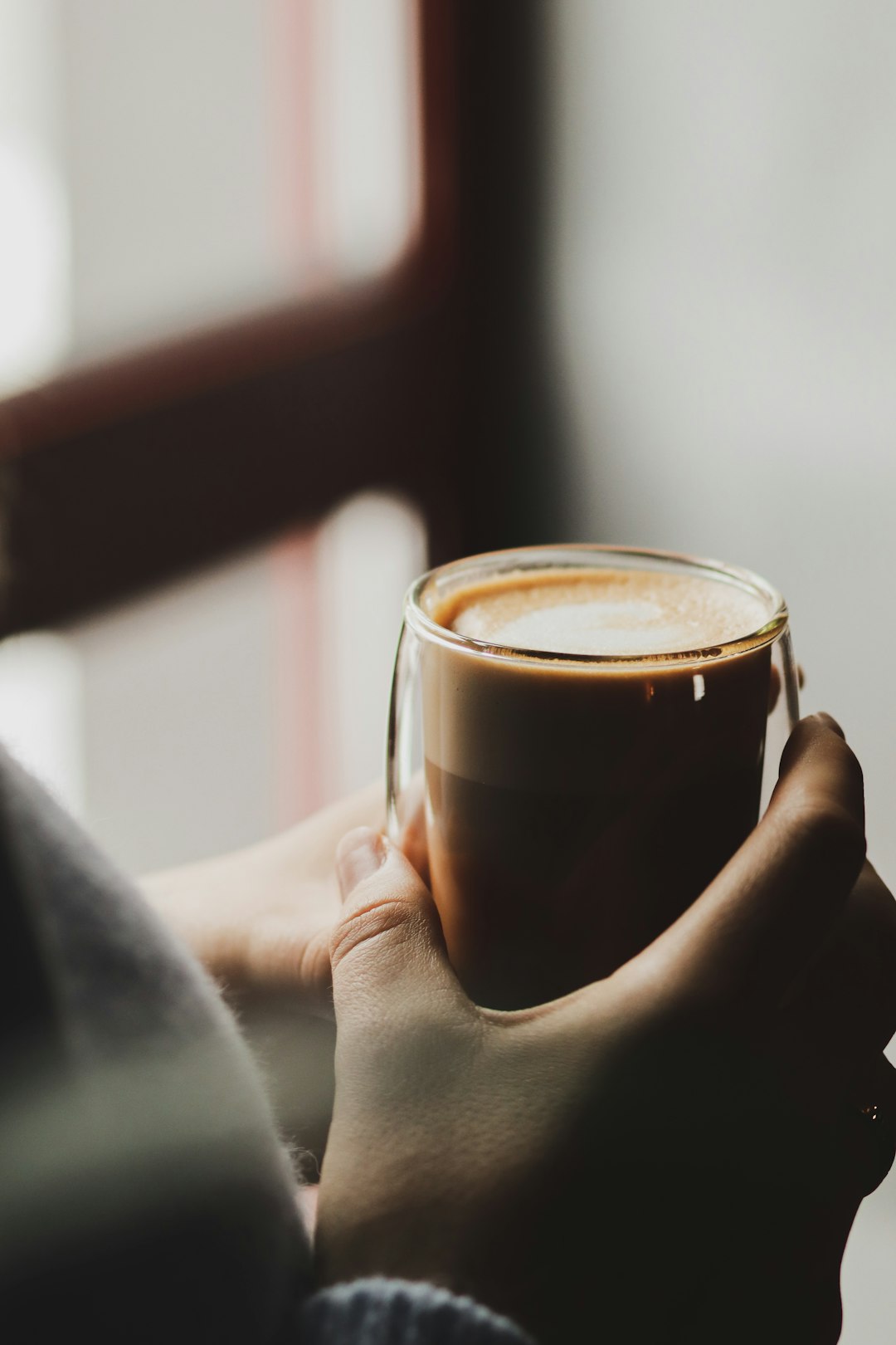 person holding clear glass mug with brown liquid