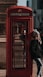 woman in black fur coat standing beside red telephone booth