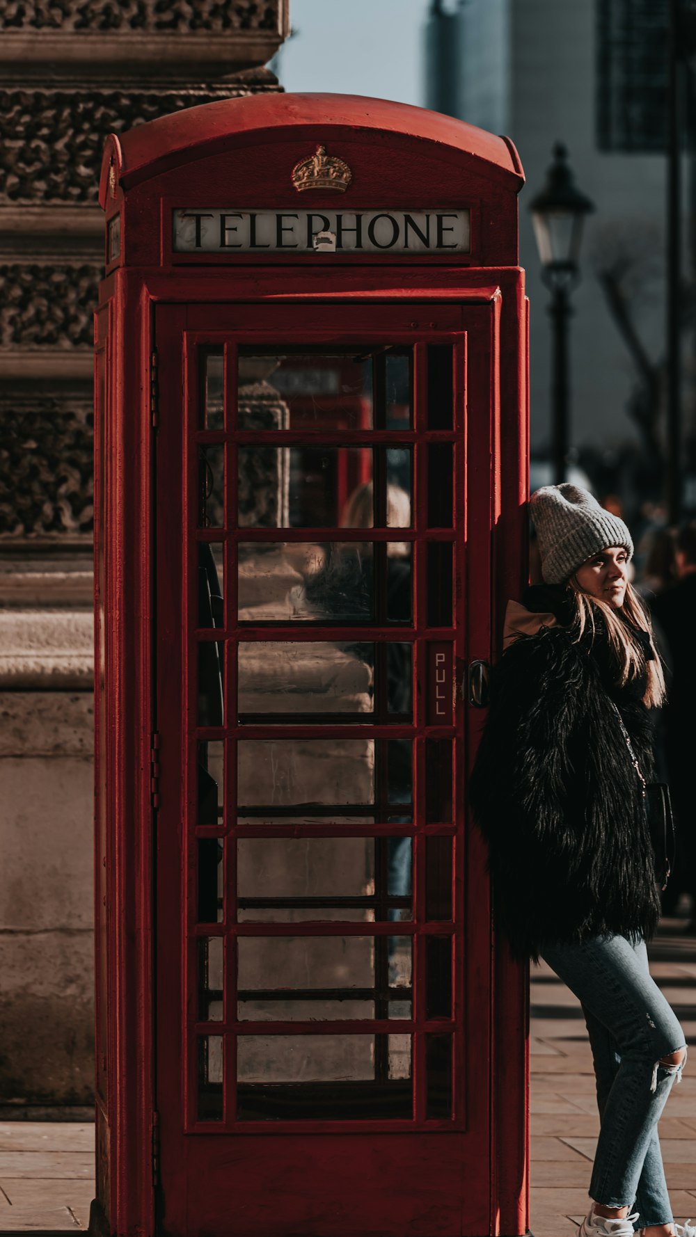woman in black fur coat standing beside red telephone booth