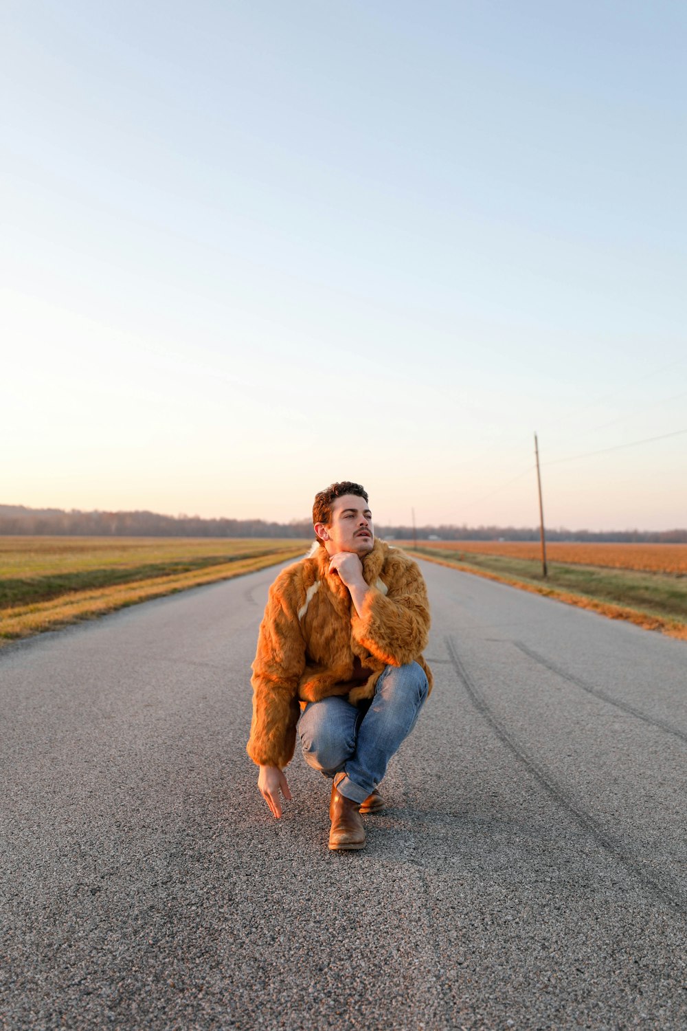 man in brown jacket sitting on road during daytime