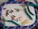 A collection of colorful beads and jewelry-making tools are arranged on a soft surface. Three pairs of pliers with teal handles are scattered around. Various beads, including shiny flower-shaped ones and small square orange beads, are organized in groups. A bunch of golden head pins are also visible.