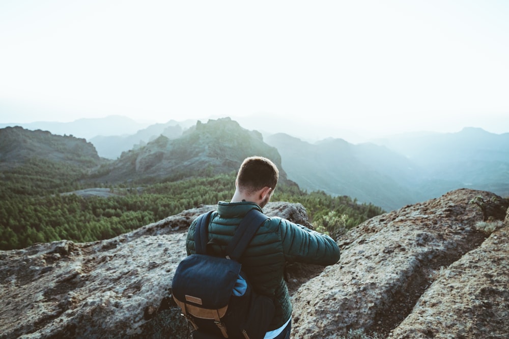 man in black jacket and blue backpack standing on rocky mountain during daytime