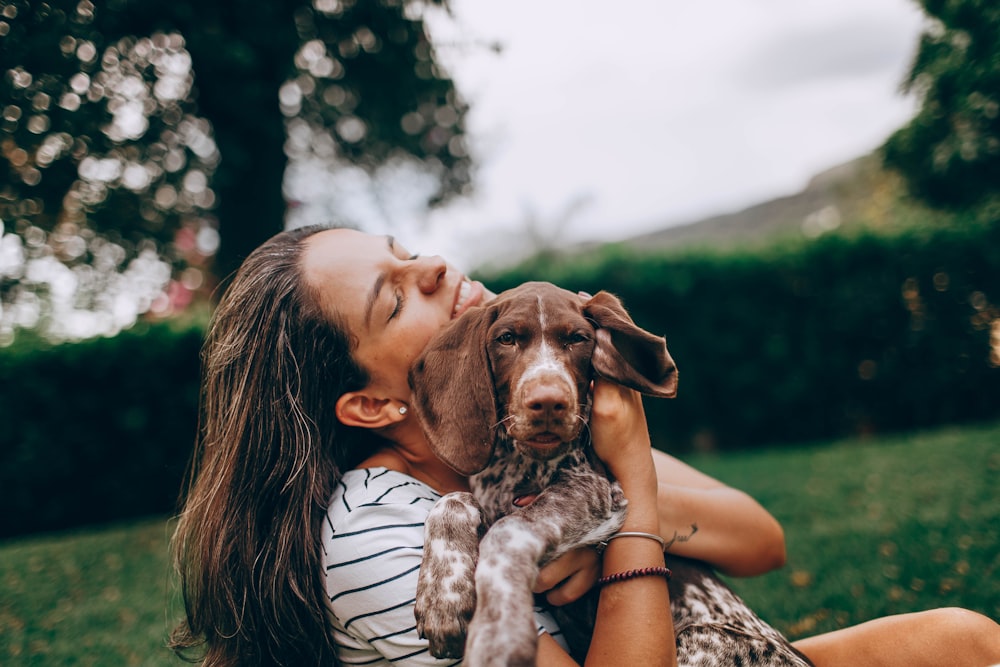 woman in white and black stripe tank top hugging brown and white short coated dog