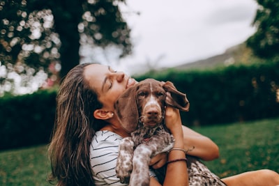 A young woman affectionately hugging her dog outdoors in a green setting