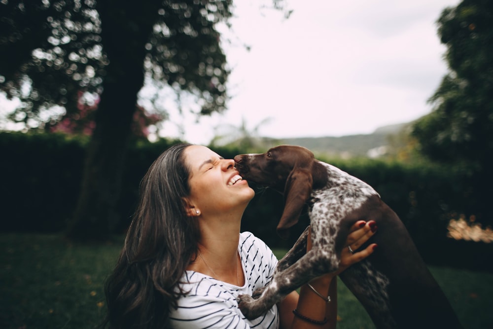 woman in white shirt kissing the black and white short coated dog
