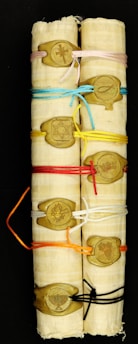 Two rolled parchment scrolls are tied with various colored strings, each secured with a wax seal. The seals feature different symbols including a cross, Star of David, fish, crown, flame, and menorah.