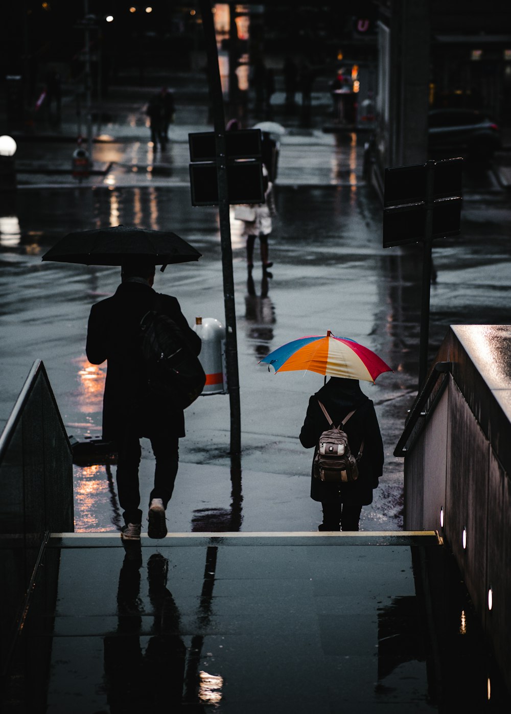 Persona con abrigo negro sosteniendo paraguas de pie en la acera durante la noche