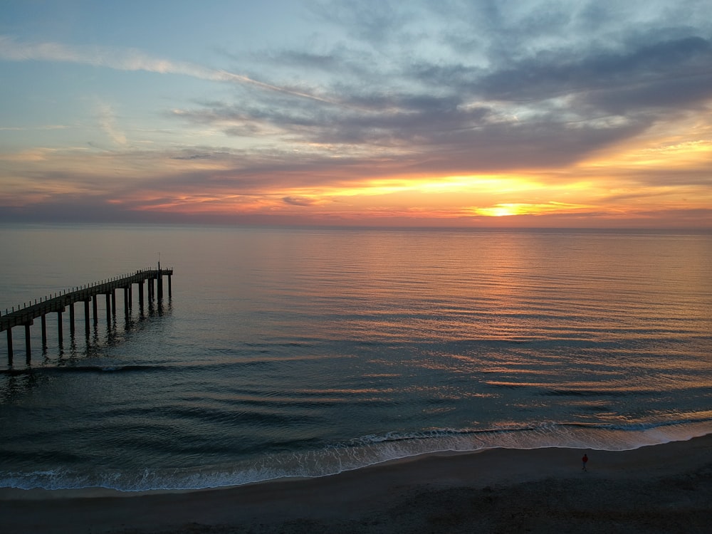 silhouette of wooden dock on sea during sunset