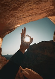 person in black long sleeve shirt raising hand in front of brown rock formation during daytime