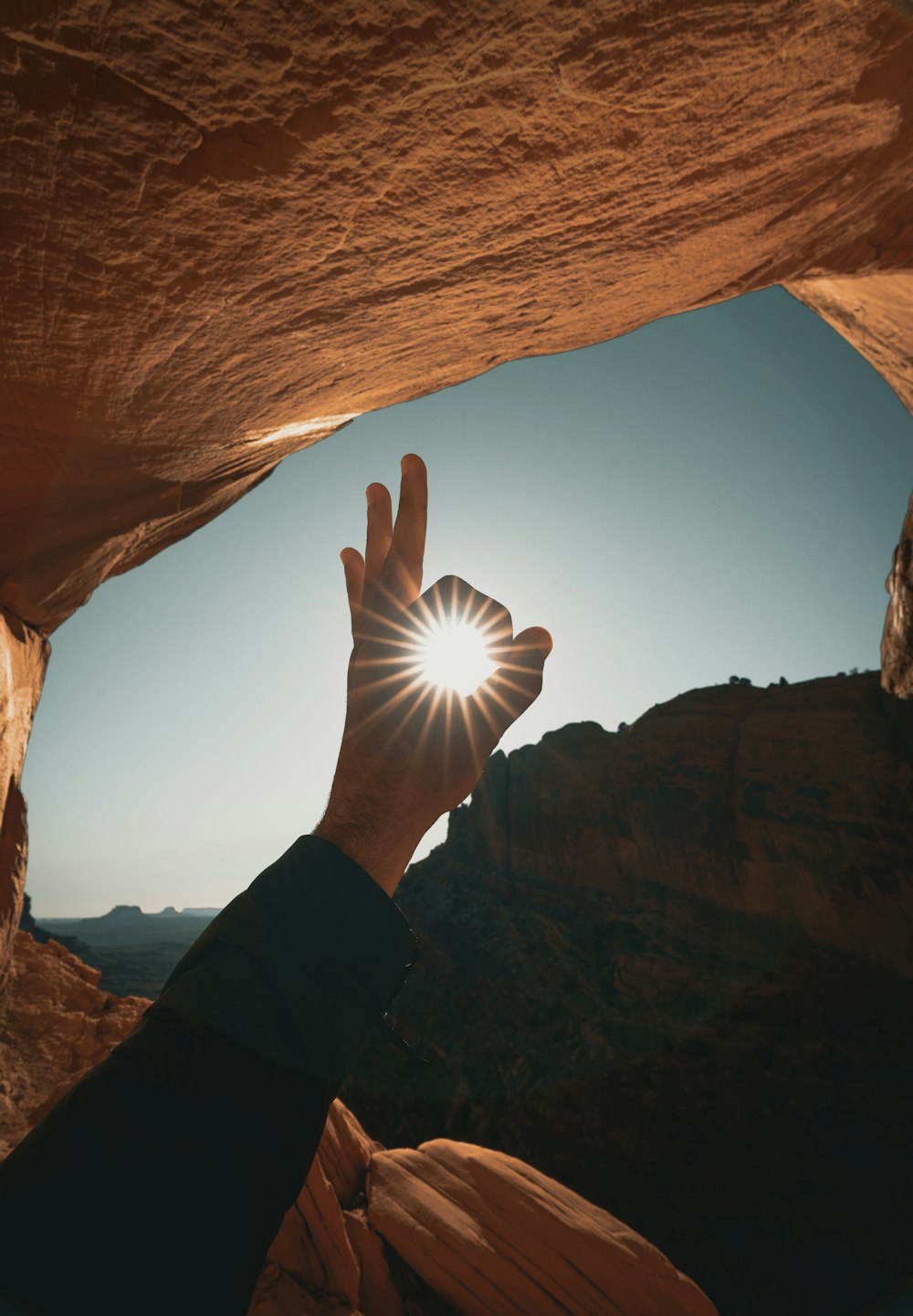 person in black long sleeve shirt raising hand in front of brown rock formation during daytime