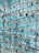 A collection of various locks attached to a grid of metal wires, with some locks displaying engraved or written messages. The grid is set against a teal-colored background, and the locks vary in color, size, and shape, including a prominent red heart-shaped lock.