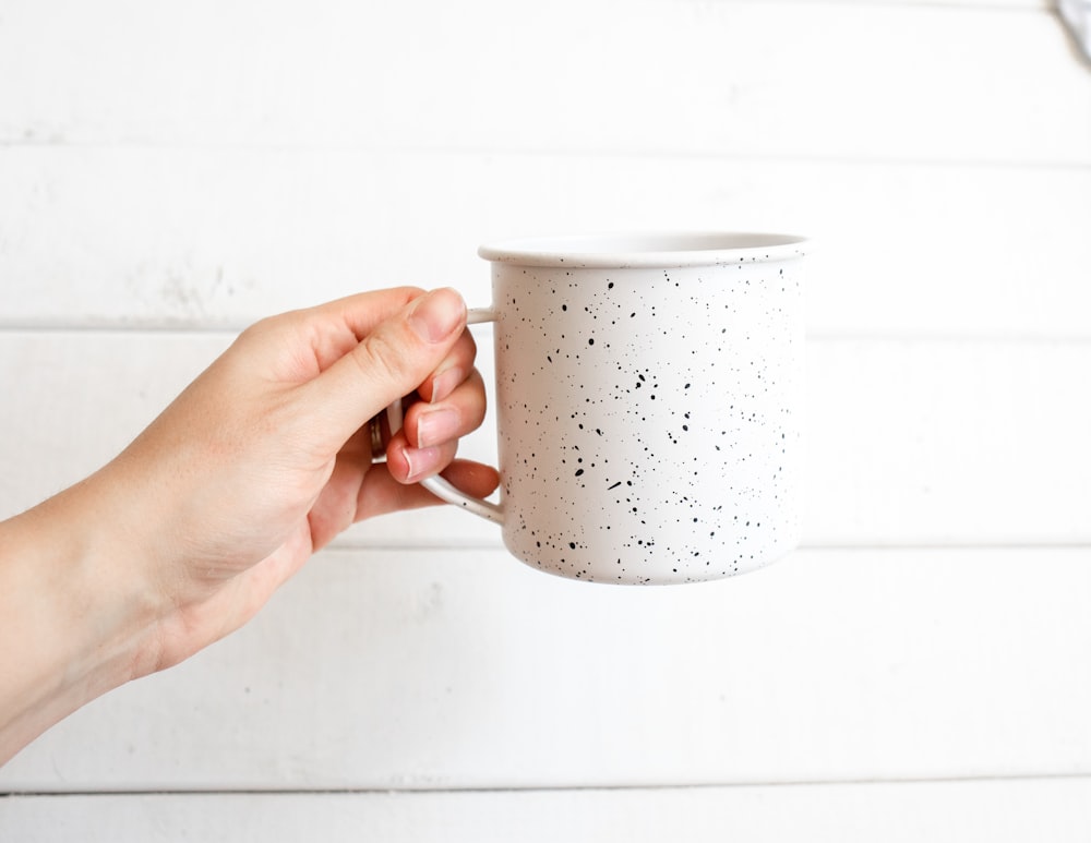 person holding white and black ceramic mug