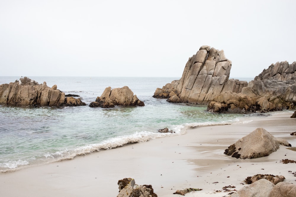 a sandy beach with rocks in the water