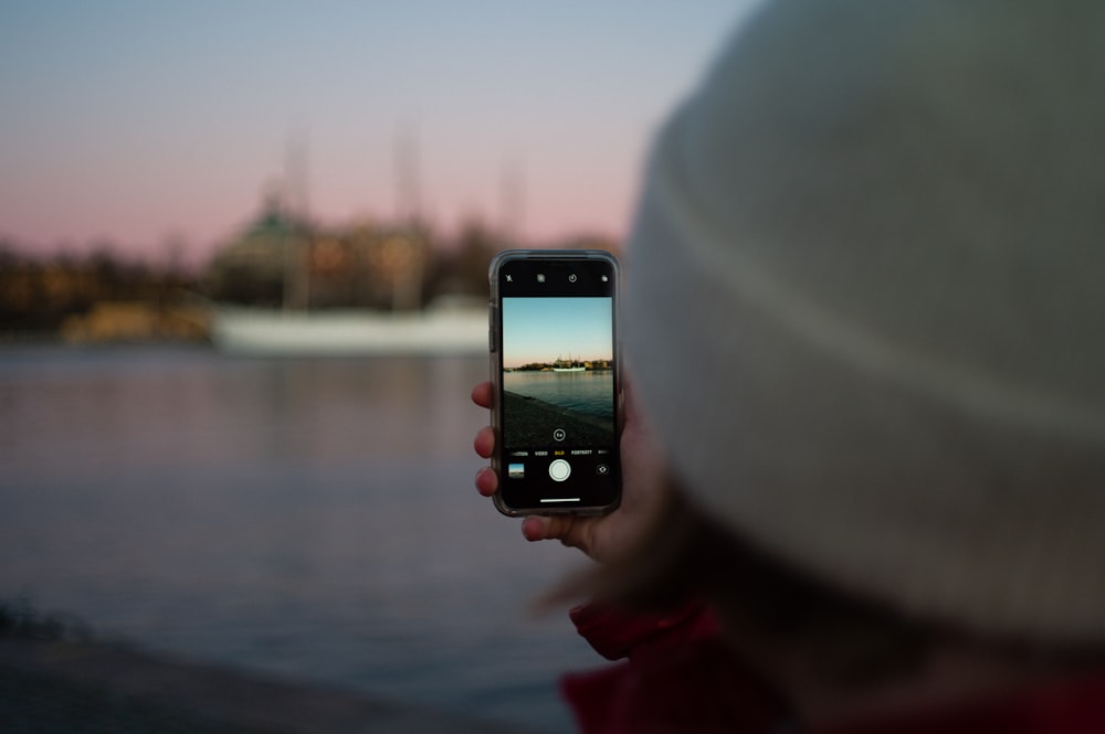 person holding black iphone 4 taking photo of body of water during daytime