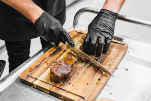 Chef’s hands seasoning freshly cut steak with spices in a rustic kitchen.