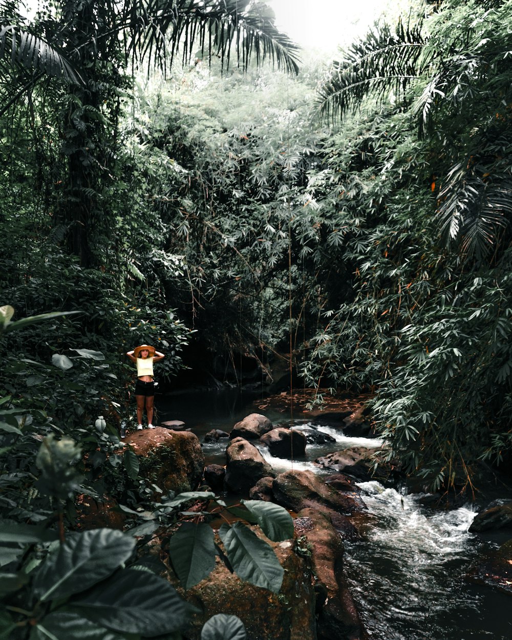 person in brown jacket sitting on rock in the middle of river