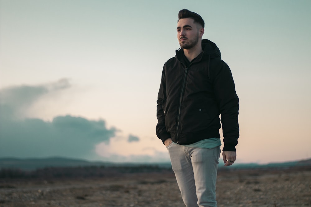 man in black jacket and white pants standing on brown field during daytime