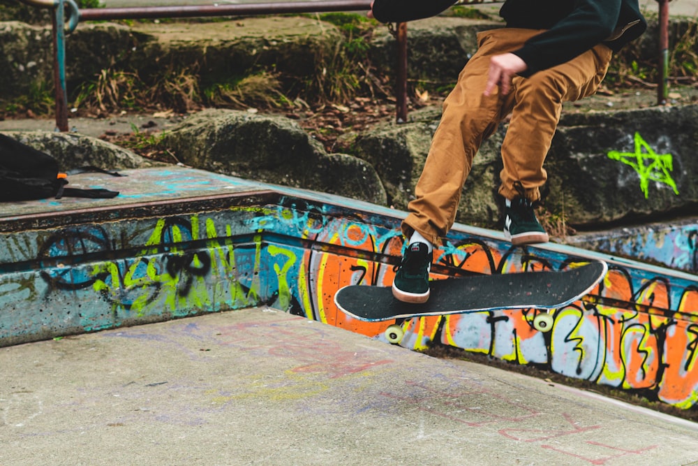 person in brown pants and brown pants riding orange and black skateboard during daytime