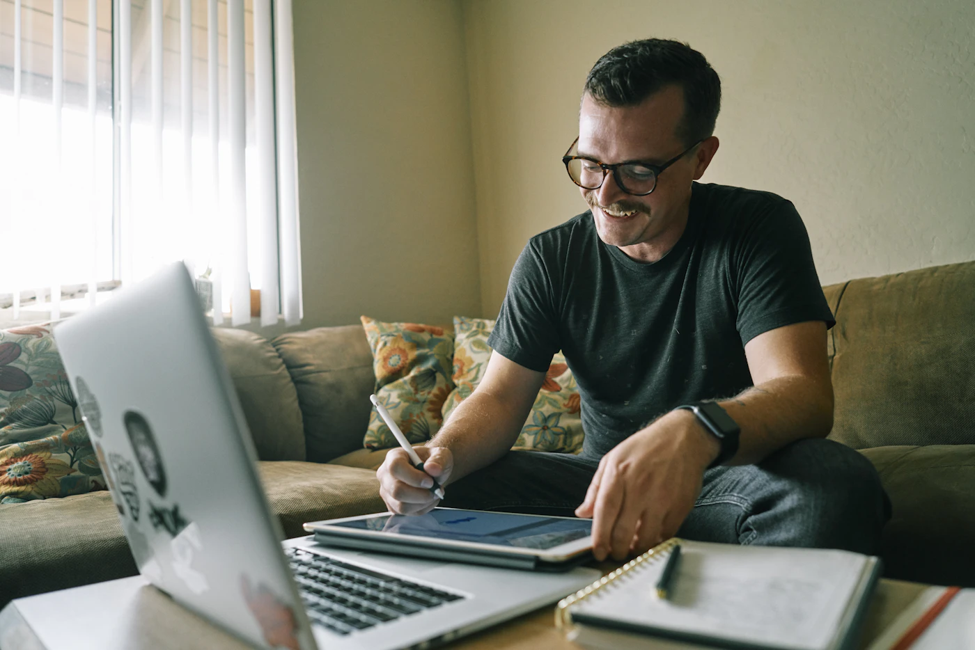 Man working on a laptop and tablet from his living room couch