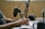 A close-up of a person typing on a keyboard, with a professional microphone and a pop filter prominently positioned in the foreground. Nearby, a pair of headphones rests on the desk. The scene suggests a podcast or audio recording setup.