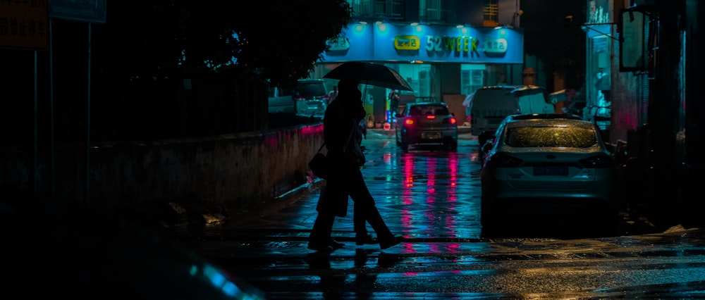 person in black jacket and pants holding umbrella walking on sidewalk during night time