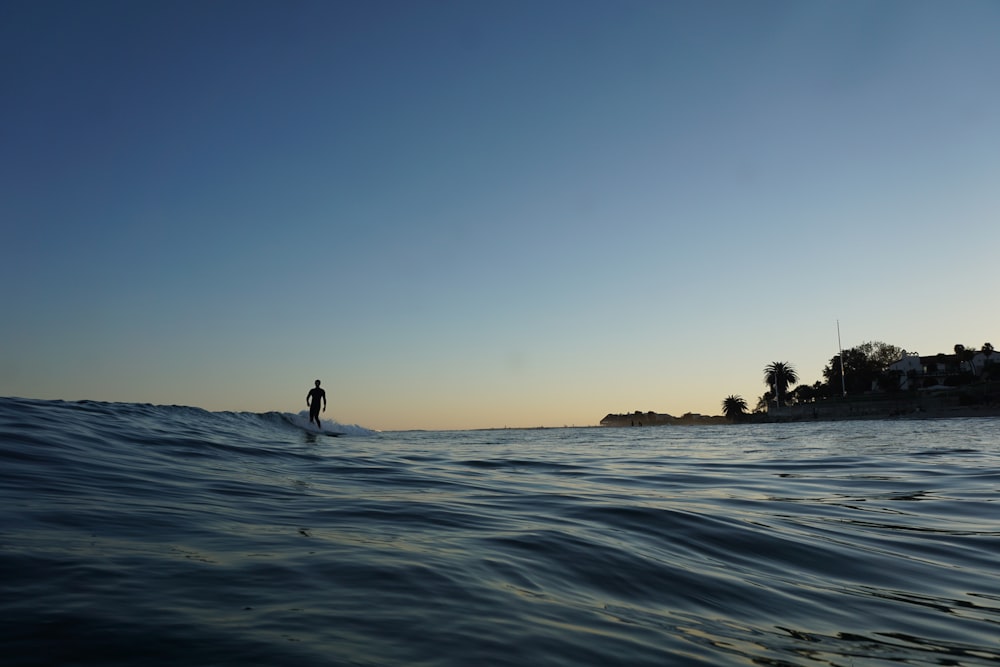 silhouette of man standing on rock formation in the middle of sea during daytime