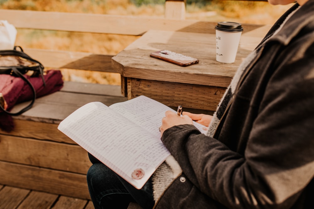 Person im grauen Mantel mit Stift und Buch