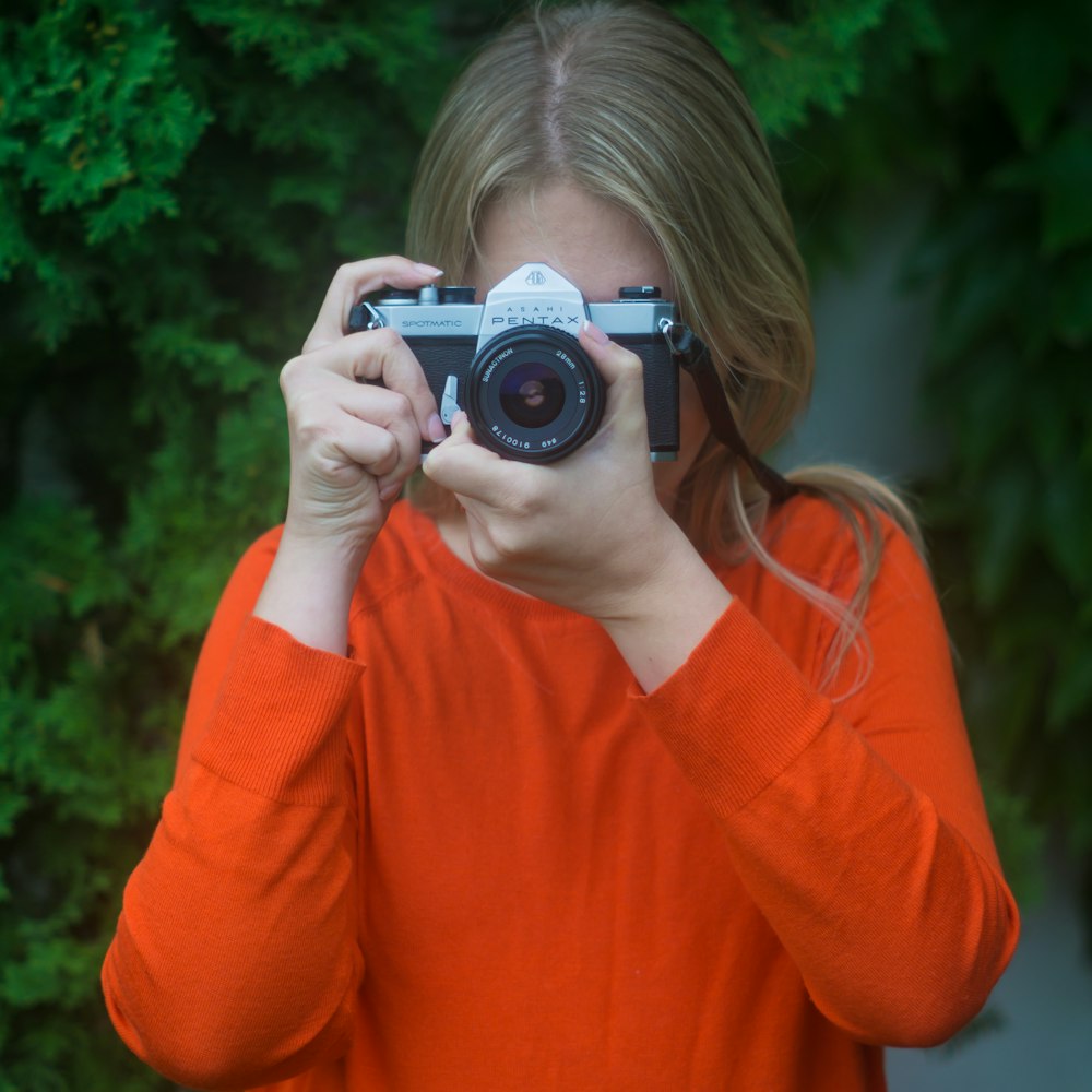 woman in orange long sleeve shirt holding black and silver camera