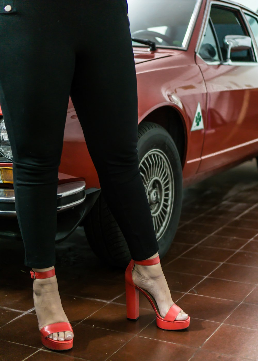 person in black pants and red shoes standing beside red car