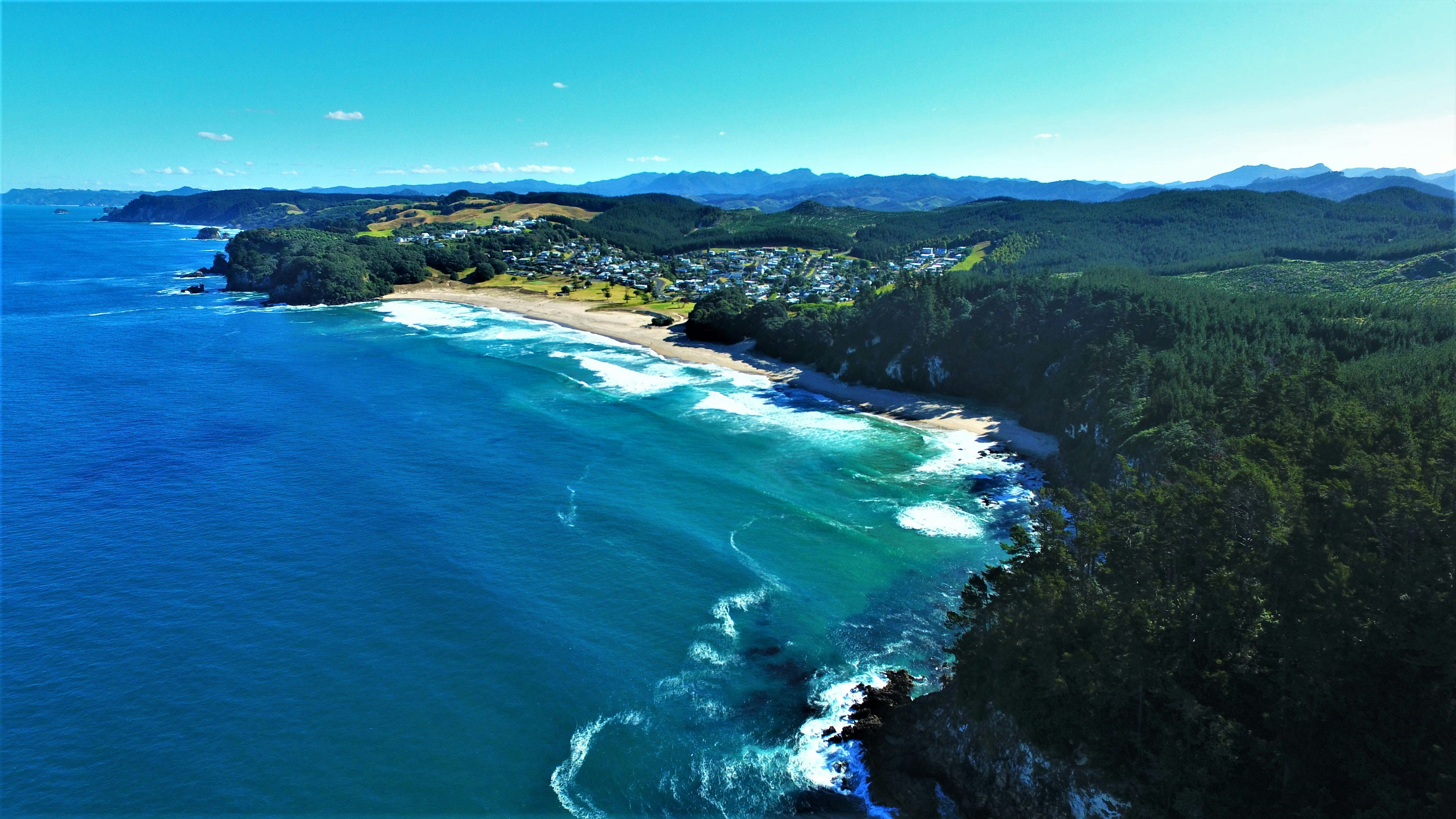 Aerial view of a stunning luxury coastal destination with turquoise water, white sandy beaches and lush green hills under bright sunlight