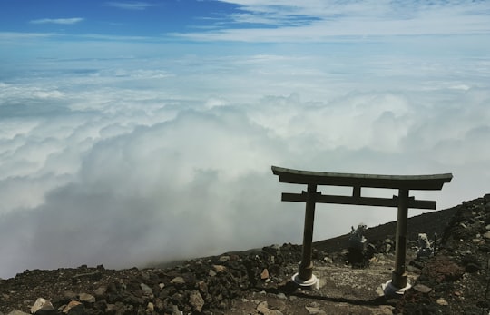 brown wooden bench on rocky shore under white clouds and blue sky during daytime in Mount Fuji Japan