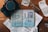 An arrangement of travel-related items including a Sony camera, an open passport with numerous stamps, flight tickets, and a pair of eyeglasses on a wooden surface.