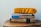A stack of books and a magazine is topped with a bright yellow cushion. The titles visible include a guide to Puerto Rico and an adventure guidebook. The books are placed on a wooden surface with natural wood grain visible.
